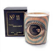 A single eye with blue rings candle with a wooden veneer, labeled 'No 11 Bergamot', alongside its black box packaging.